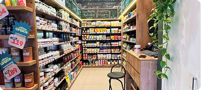 Interior de loja com prateleiras cheias de produtos naturais e suplementos organizados em corredor estreito.